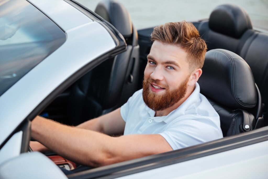 joyful-man-driving-convertible-and-gazing-at-camera-SBI-302779420-1